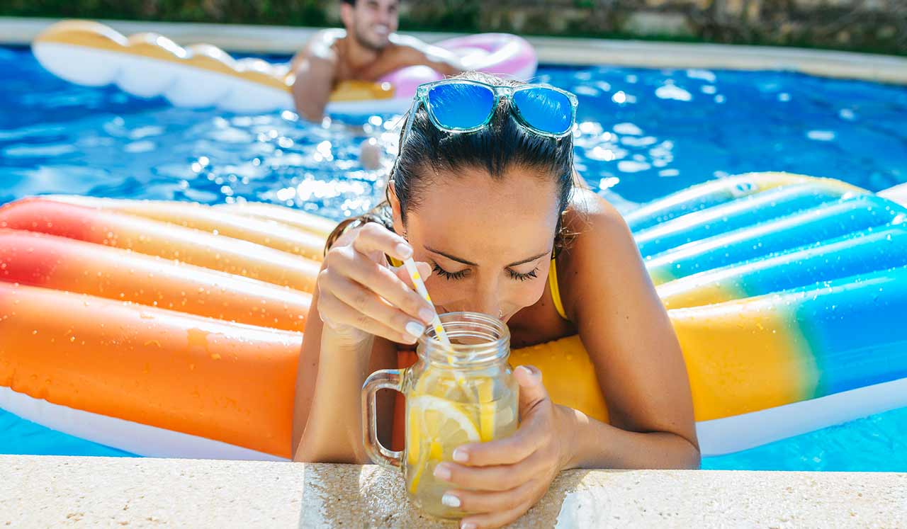 A woman on a colorful raft in a pool, sips from a mason jar.