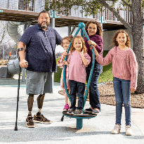 TIRR Memorial Hermann Osseointegration patient, Alex, stands with his four daughters at a play ground.