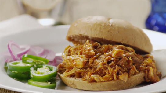 A plate featuring a pulled-chicken sandwich with barbecue sauce and a side of jalapenos and red onions.