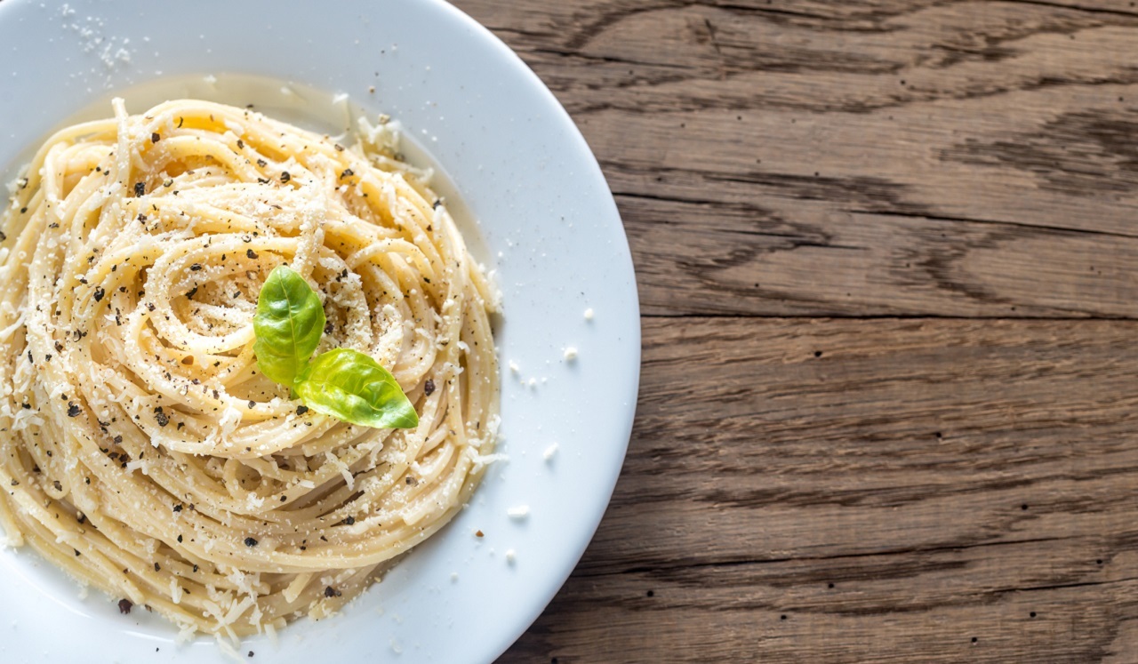 An aerial view of plated spaghetti noodles sprinkled with pepper and parmesan cheese.