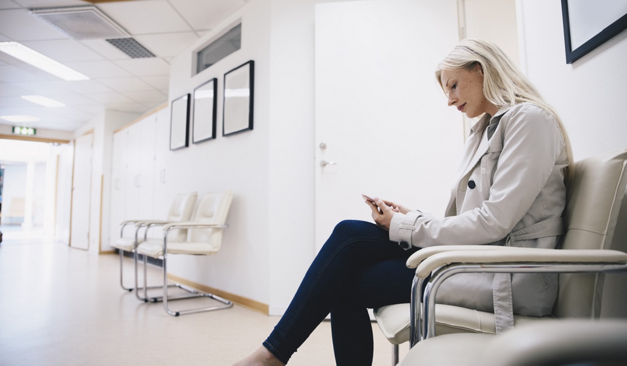 A woman looking at her phone while in the waiting area of a doctor's office.