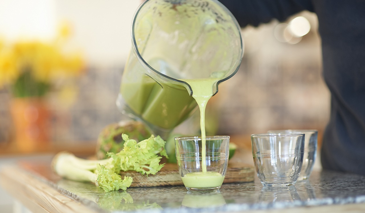 Celery juice being poured from a blender into a small glass.