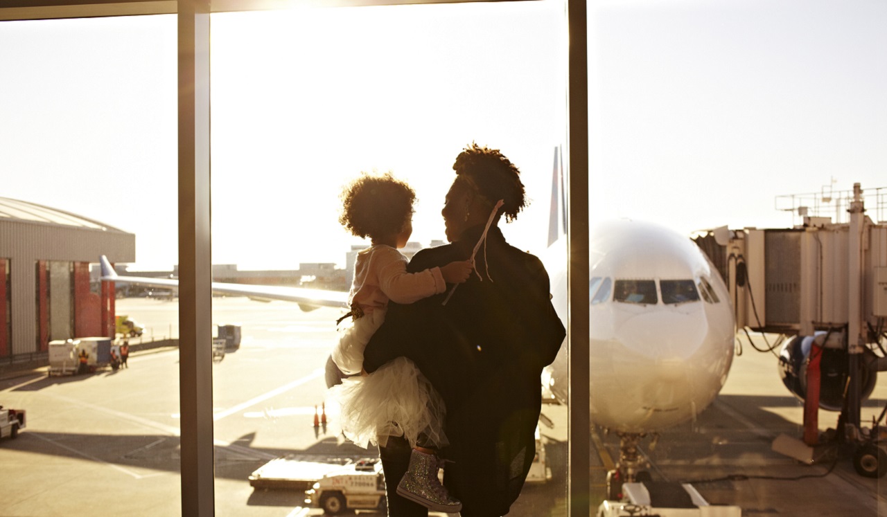 A person holding a child looking at an airplane at the airport.