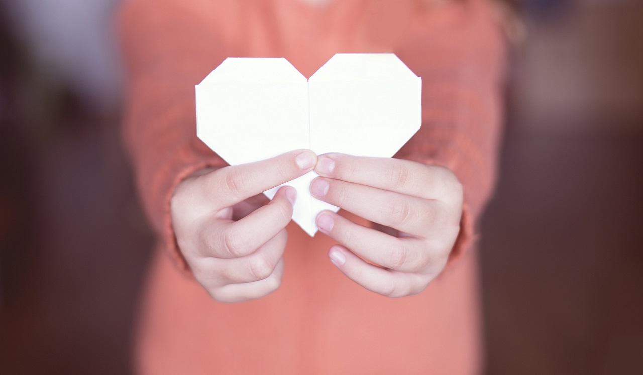 A pair of hands holds up a paper heart.