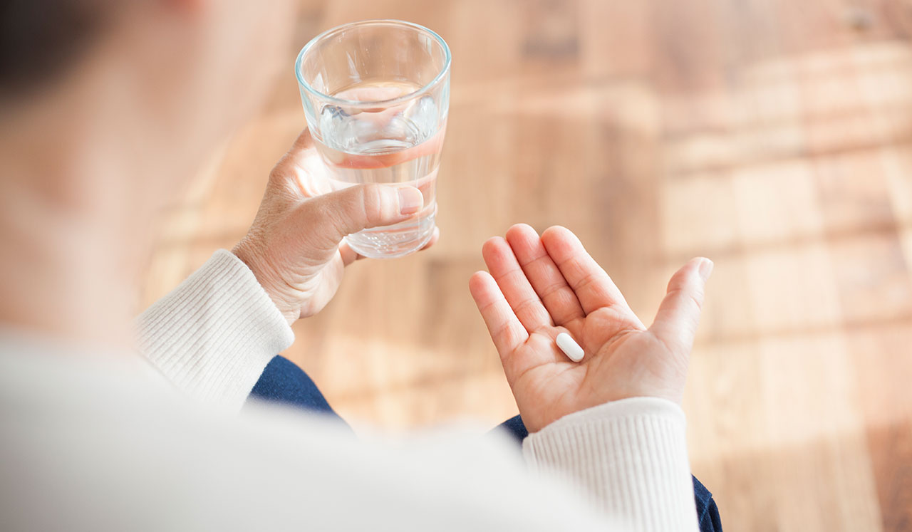 Person holding a water glass and a pill