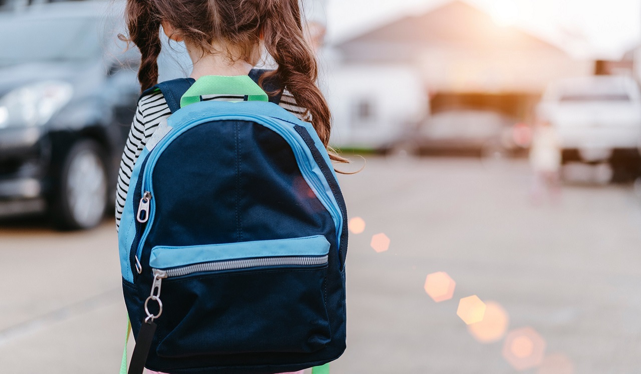 A small child in pigtails wears a blue and black back pack.