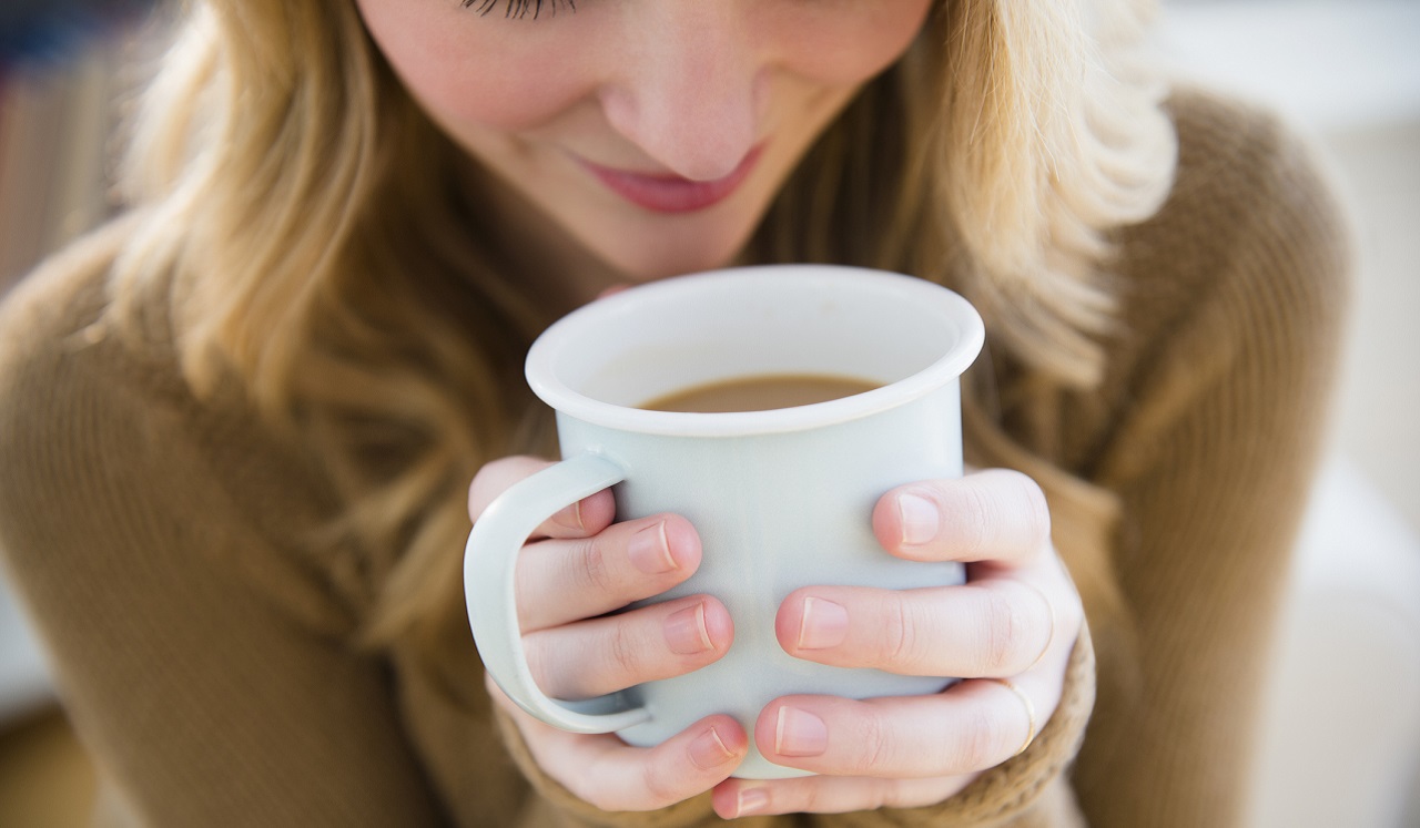 A woman holds a cup of coffee, breathing in the aroma.