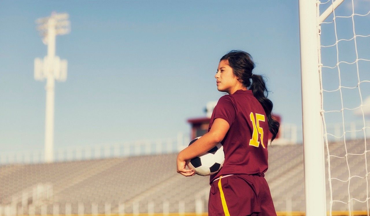 A teenage girl in a sports uniform holding a soccer ball.