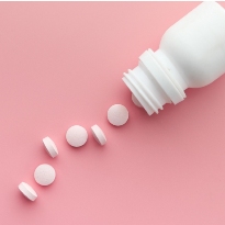A white bottle lays on its side, spilling white pills in a line along a pink background.