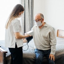 In a hospital setting, a clinician checks the blood pressure of a masked patient.