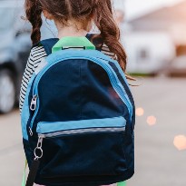 A small child in pigtails wears a blue and black back pack.