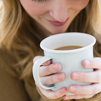 A woman holds a cup of coffee, breathing in the aroma.