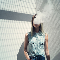 A teenage girl with smoke leaving her mouth and obscuring her face.