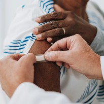 Person placing bandaid on arm after vaccine