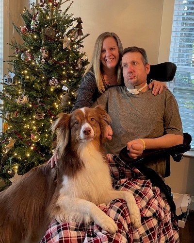 Eric Smith, a TIRR Memorial Hermann patient, sits with his wife and dog in front of a Christmas tree.