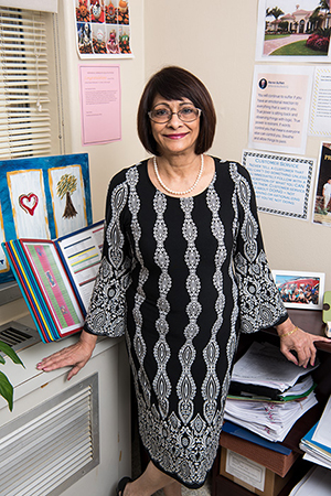 Faizbano Rayani smiles, standing by her work desk adorned with letters and pictures.
