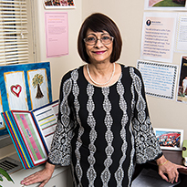 Faizbano Rayani smiles, standing by her work desk adorned with letters and pictures.