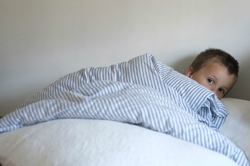 Child hiding underneath bed sheets