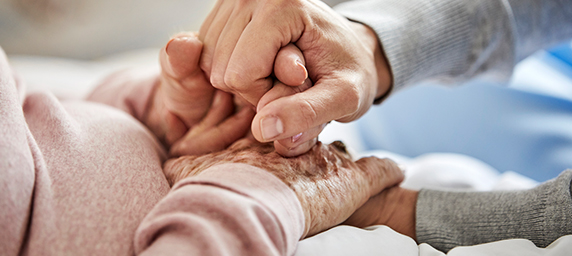 An elderly pair of hands being held earnestly by another's hands.