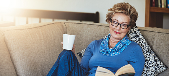 A woman reclines while enjoying a book on the couch