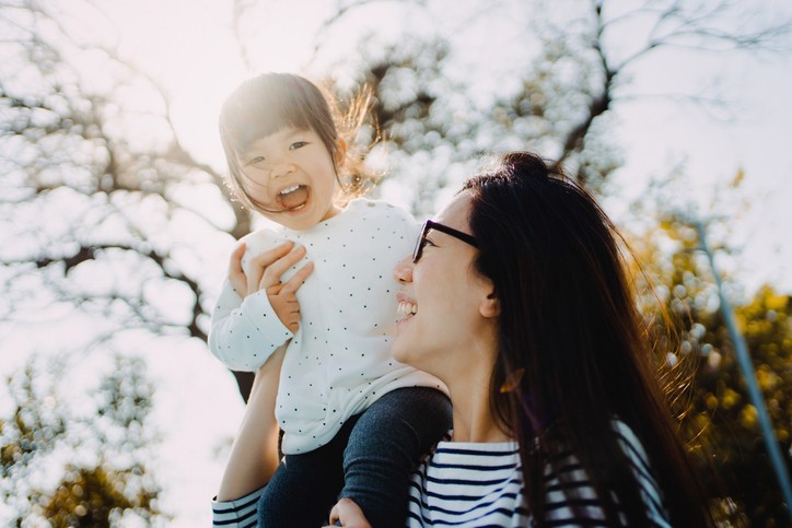 Young Asian mother bonding with her adorable little daughter, having fun and smiling joyfully in the park